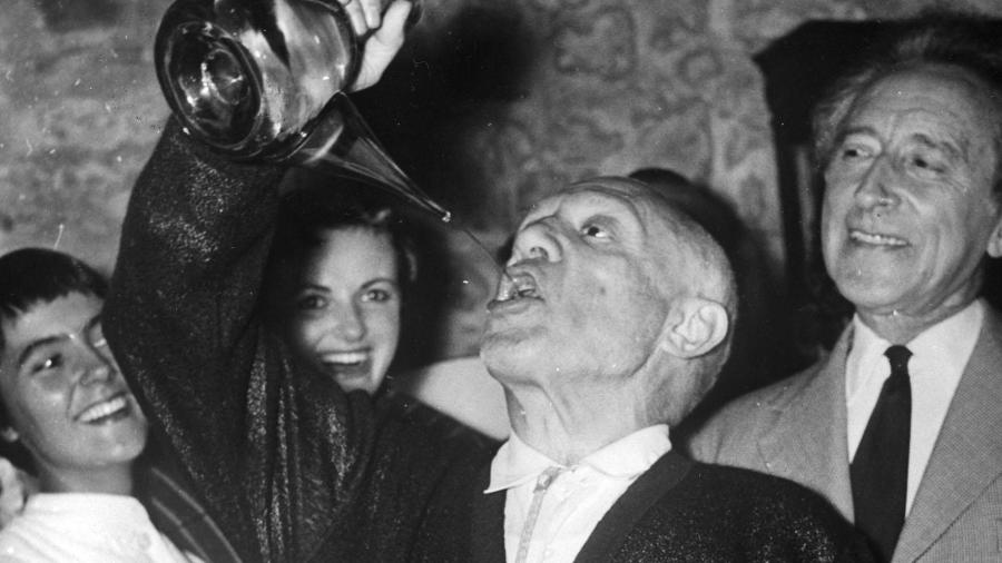 Pablo Picasso bebe vinho ao estilo espanhol, em seu aniversário de 75 anos. Ao seu lado, o poeta francês Jean Cocteau - PA Images via Getty Images