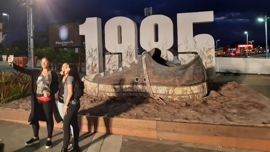 Fãs fazem selfie em frente a tênis com lama que integra a cenografia da Rota 85, no Rock in Rio