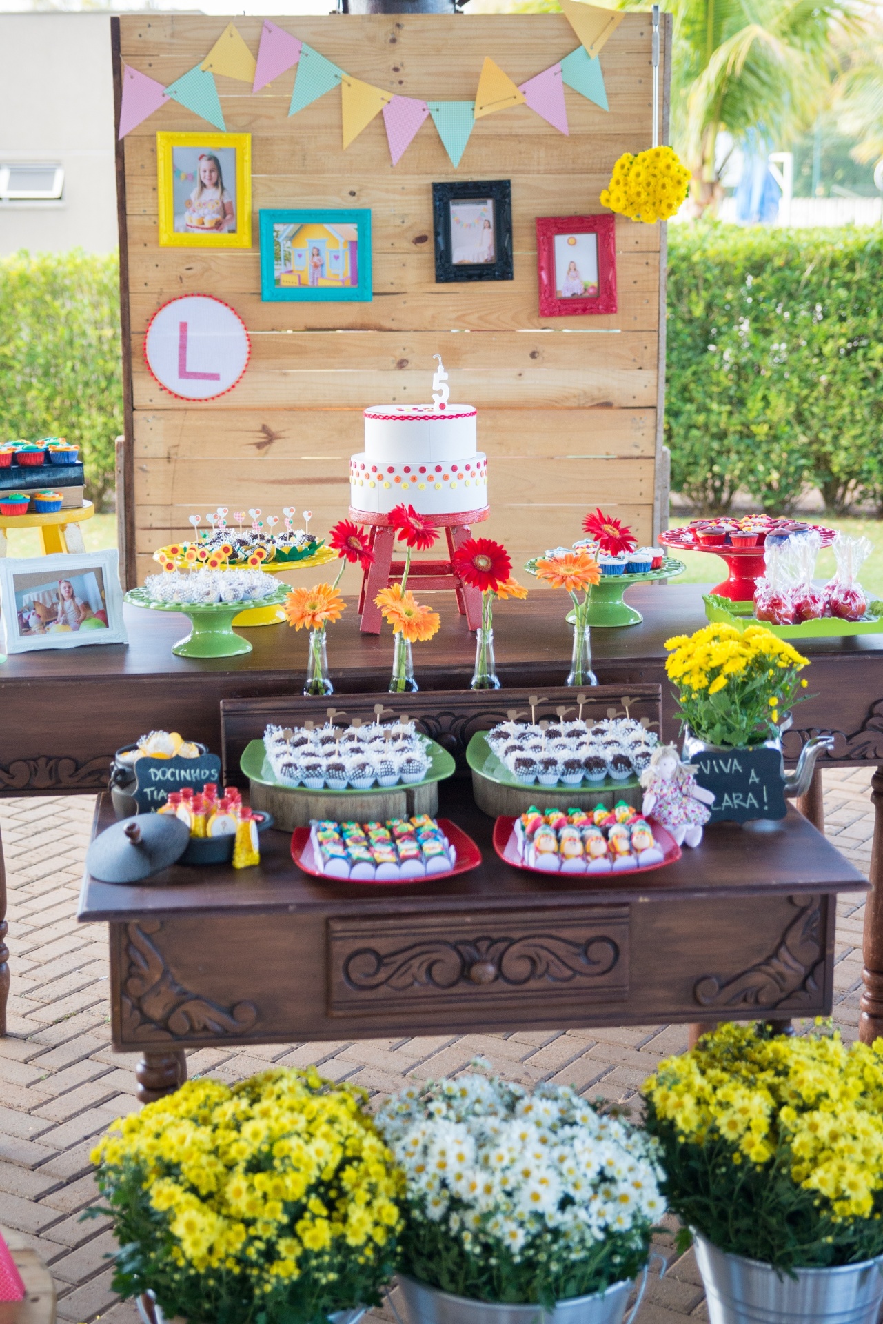 Samambaias, gérberas, pinóquio amarelo e margaridas foram as flores utilizadas para decorar a mesa do aniversário com o tema do Sítio do Picapau Amarelo. O painel atrás da mesa do bolo foi feito com duas placas de pallet e várias fotos da aniversariante foram colocadas para criar um clima de "casa da vovó" - Karl Ellwein/Dueto em Versos/Divulgação