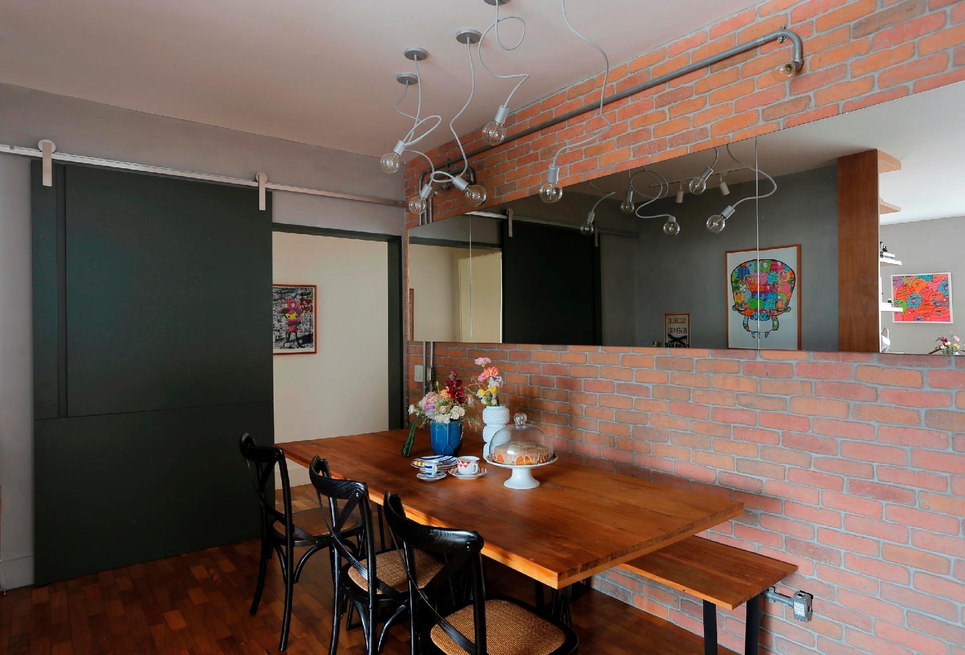 Uma atmosfera descolada, mas também acolhedora. Era esse o objetivo do projeto da arquiteta Paula Neder, que utilizou para isso madeira maciça de demolição na mesa, tijolinhos aparentes e, para complementar a pegada industrial, apostou nas tubulações elétricas a mostra, assim como nas luminárias que lembram gambiarras. Cadeiras pretas criam um ponto de destaque em meio à tonalidade amarronzada - Leonardo Costa/Divulgação