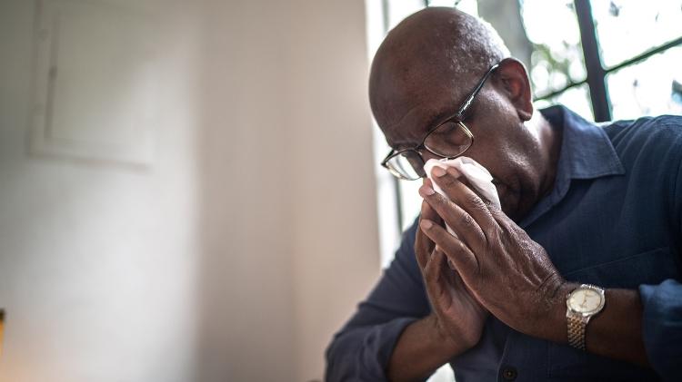 Homem idoso assoando o nariz, limpando, espirrando, gripe, influenza, resfriado, covid - iStock - iStock