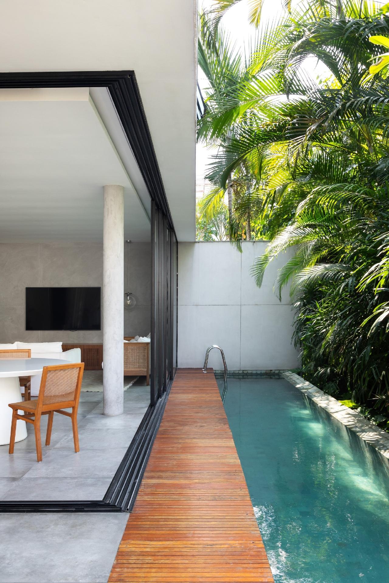 No piso térreo, os pilares da fachada foram deslocados para viabilizar a abertura total das esquadrias piso-teto e integrar ao máximo a área social com cozinha integrada e a área externa. Ali foi construída a raia, que também funciona como espelho d'água e refresca a casa, com muro verde ao fundo. - Luiza Schreier/Divulgação