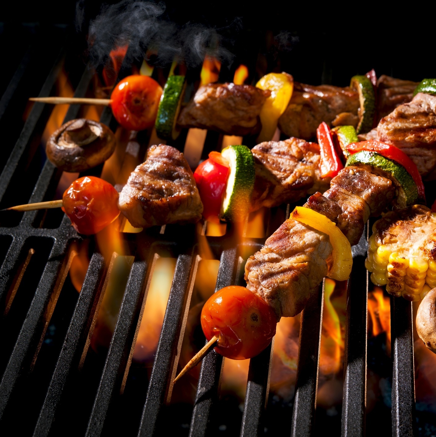 A imagem mostra uma churrasqueira acesa e lotada de espetos de carne para  um suculento churrasco.Tanto o Brasil quanto o…