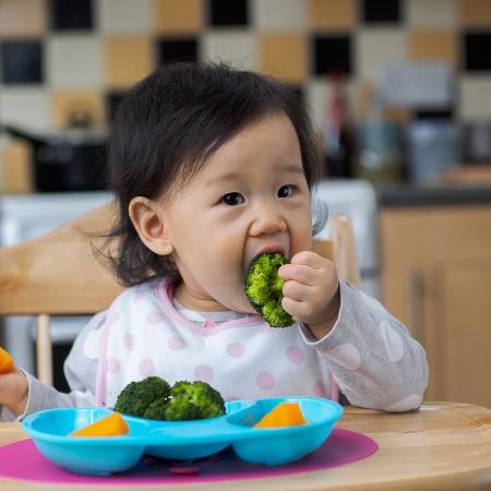 Criança asiática comendo brocólis - Istock