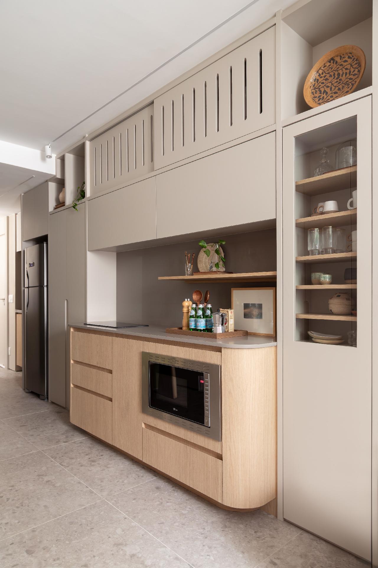 Antes da reforma, na entrada do imóvel havia uma bancada com uma cuba minúscula e um espaço para fogão de uma boca - estava ali a cozinha - seguida de um corredor estreito, sem utilidade. "Embora a cliente não cozinhe com frequência, pediu um espaço mais confortável para isso", diz Marina. As curvas no mobiliário e o projeto tornaram possível caber bancada para cooktop, forno multiuso e airfryer. - Lilia Mendel/Divulgação