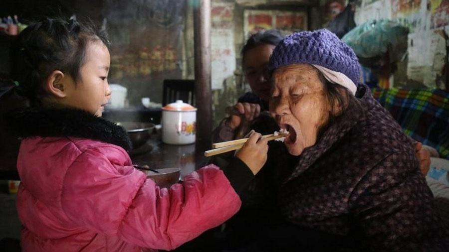 A menina chinesa Anna Wang alimentando a bisavó, enquanto a avó observa - Reprodução/Bored Panda