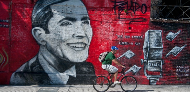 Rapaz pedala bicicleta em frente a mural grafitado com a imagem do compositor de tango Carlos Gardel, em Buenos Aires - Patricio Murphy/Zumapress