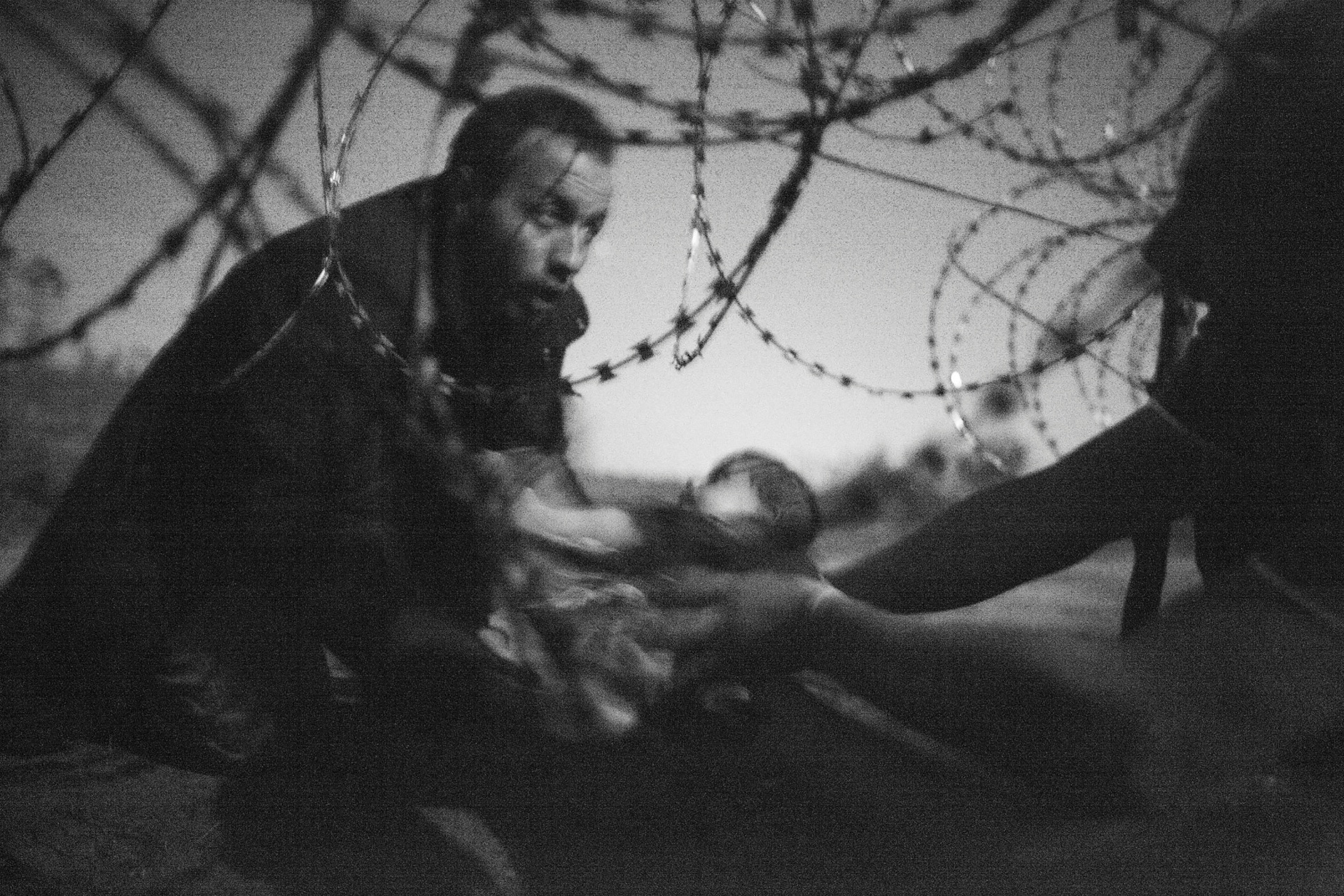18.fev.2016 - A fotografia que ganhou o prêmio World Press Photo (WPP), do australiano Warren Richardson. A imagem em branco e preto mostra um homem passando um bebê através de uma cerca de arame na fronteira entre a Sérvia e a Hungria. - Warren Richardson/World Press/EFE