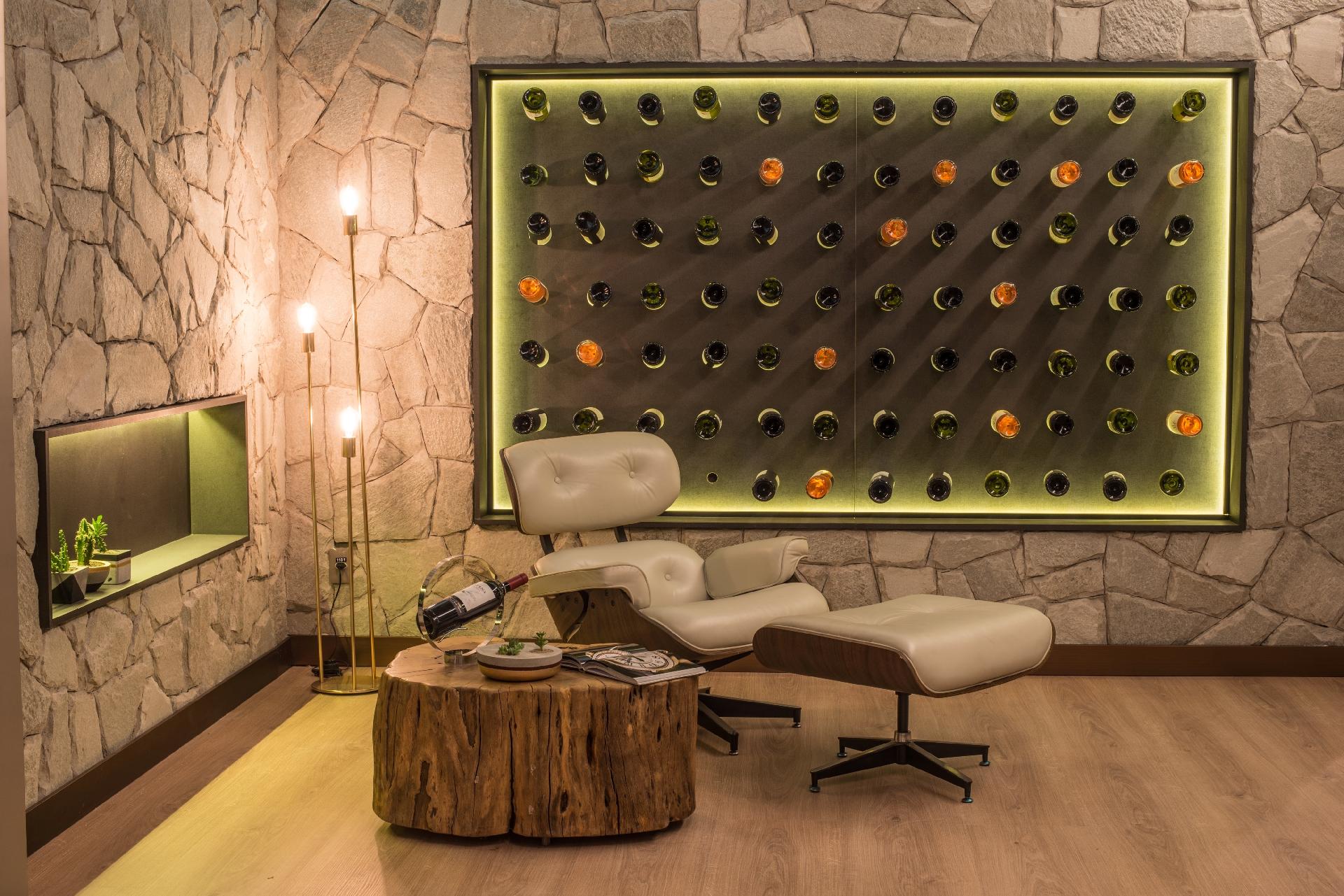 Casa Cor MT 2016 - Vinho ao alcance da poltrona foi a grande sacada do Lapidário Gastronômico, idealizado por Andressa Borsato, Camila Borim e Zilda Zompero. A adega segue o padrão usado no nicho (à esq.) com luz indireta e revestimento verde. A estrutura não briga com a ambientação rústica dada pela mesa de tora e as paredes revestidas por pedras - Lucas Ninno/Divulgação