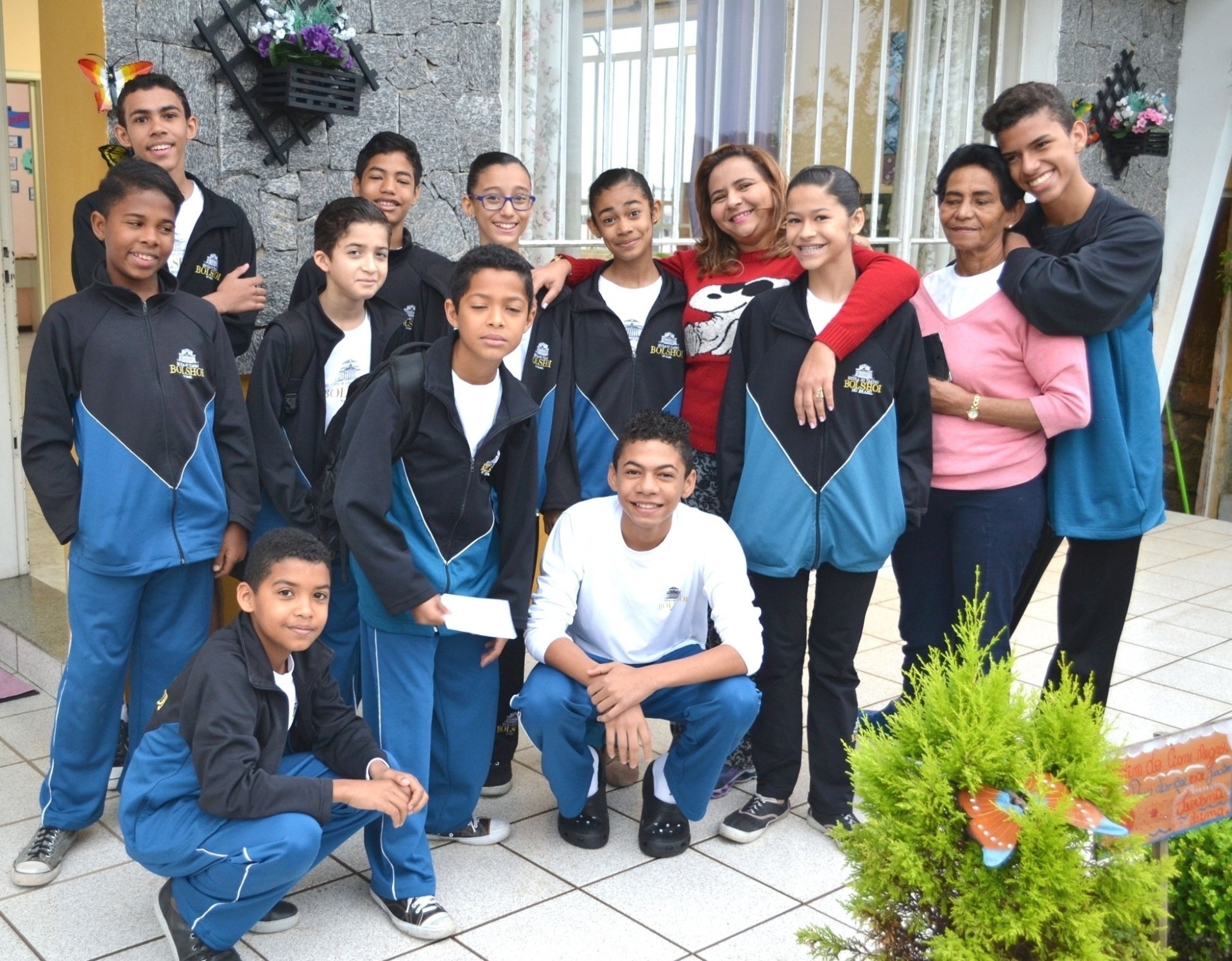 Os moradores da Casa do Piauí em meio à mãe social Rosana Gomes (de vermelho), que há um ano cuida de oito meninos e três meninas (Izabela aparece de óculos azuis) que dançam na Escola do Teatro Bolshoi, em Joinville (SC). A senhora de casaco rosa é uma prima de Rosana que a ajuda nas tarefas domésticas e na alimentação da garotada - Manuela Schneider/Bolshoi