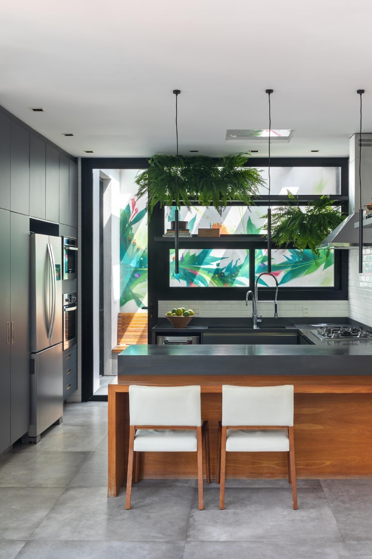 Em forma de U, a bancada da cozinha é usada no dia a dia, com espaço para refeições rápidas. Atrás dela surge um painel pintado, que tinge discretamente a vista. - Luiza Schreier/Divulgação