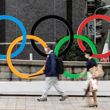 Pessoas usando máscaras contra covid-19 passam em frente aos anéis olímpicos em Tóquio, no Japão - Takashi Aoyama/Getty Images