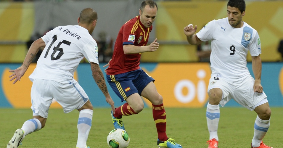 16.jun. 2013 - Iniesta tenta passar pela marcação de dois jogadores do uruguai