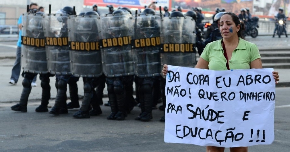16.jun.2013 - À frente de Tropa de Choque da polícia, mulher exibe cartaz em protesto contra a Copa no Brasil