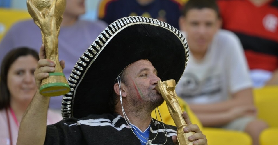 16.jun.2013 - Torcedor italiano usa chapéu mexicano para beijar uma réplica da taça Jules Rimet enquanto segura uma da Copa do Mundo no Maracanã