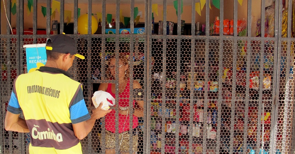 17.jun.2013 - Cristina, dona de mercadinho na favela Oitão Preto, entrega mercadoria a cliente por buraco na grade de proteção do estabelecimento: medo de assalto