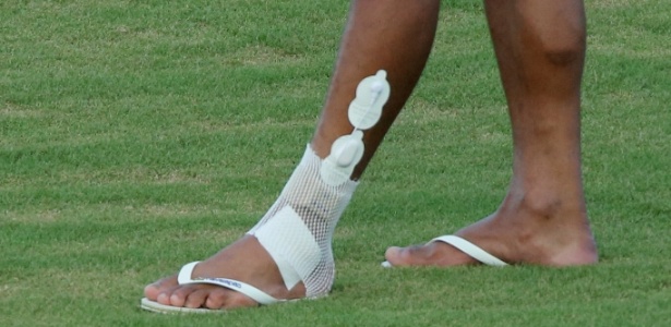 Paulinho caminha no gramado com proteção no tornozelo lesionado 