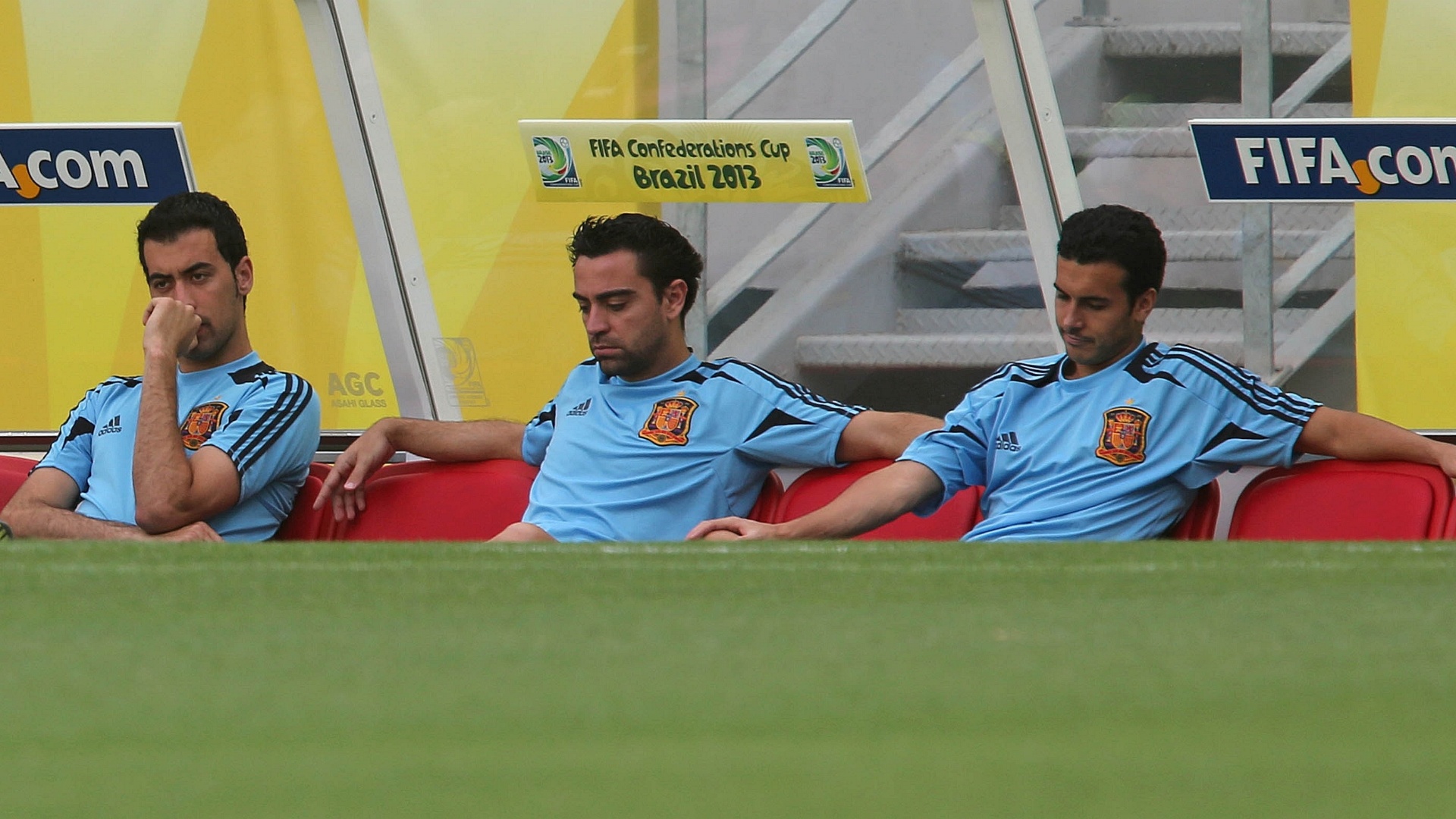 26.jun.2013 - (Da esq para dir) Busquets, Xavi e Pedro sentam no banco de reservas durante treino da Espanha