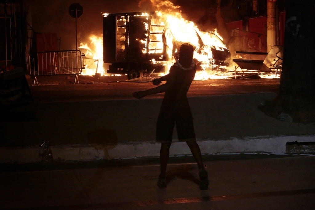 26.jun.2013 - Manifestante joga pedra contra a polícia  e observa caminhão incendiado nos arredores do Mineirão
