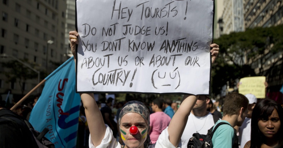 Manifestante na praça Sete de setembro carrega cartaz com frase em inglês ("Hey, turistas! Não nos julgem. Vocês não sabem nada sobre nós ou sobre nosso país", em português