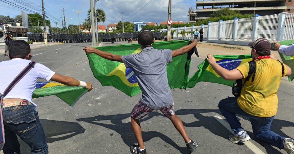 27.jun.2013 - Manifestantes esticam bandeiras do Brasil a metros de distância de barreira policial; o protesto pretende chegar ao estádio do Castelão, e a polícia tenta conter o avanço