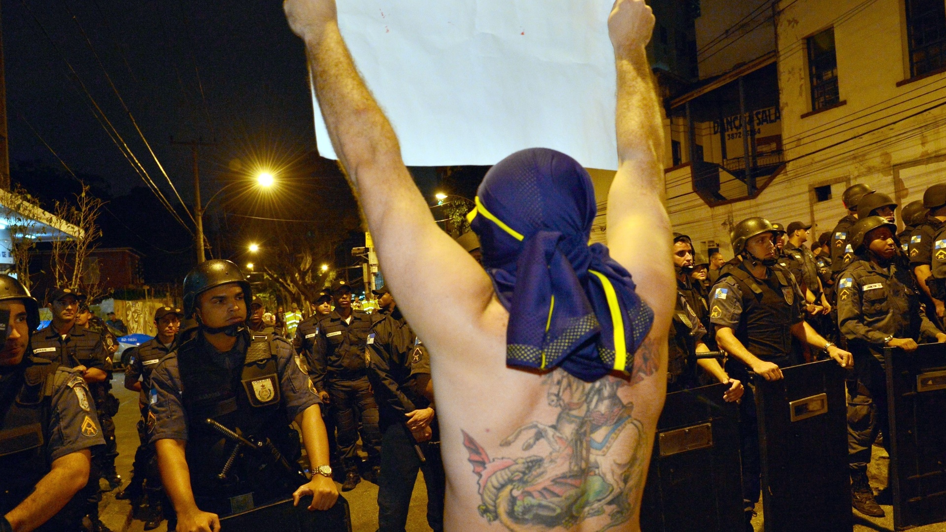 30.jun.2013 -  Manifestante levanta cartaz de protesto diante do cordão policial a caminho do Maracanã