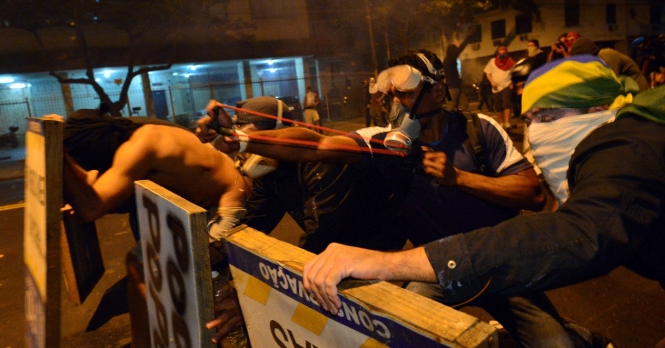 30.jun.2013 - Manifestante se esconde atrás de placas e usa estilingue para atirar contra a polícia durante protesto