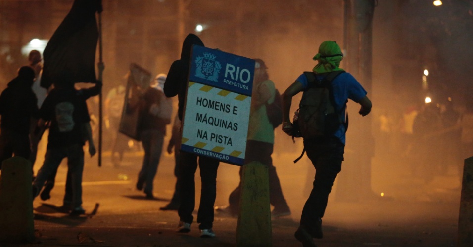 30.jun.2013 - Manifestantes correm em meio à fumaça com placa arrancada da rua