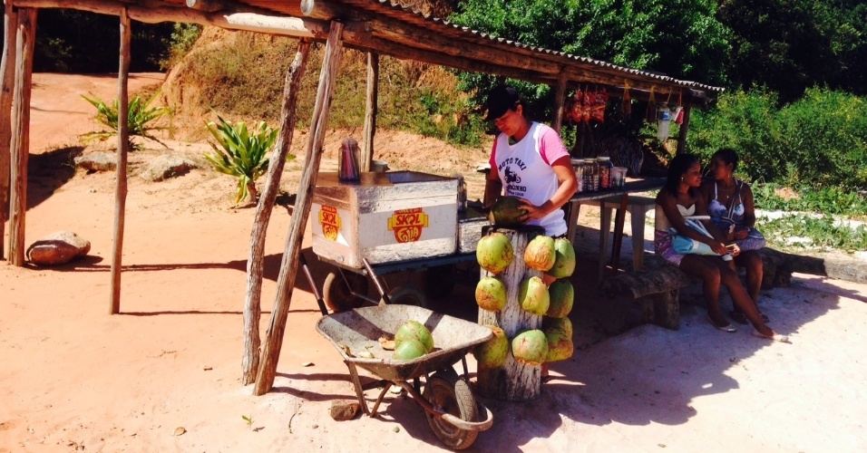 Maria corta cocos para servir os dois clientes que estão na barraca