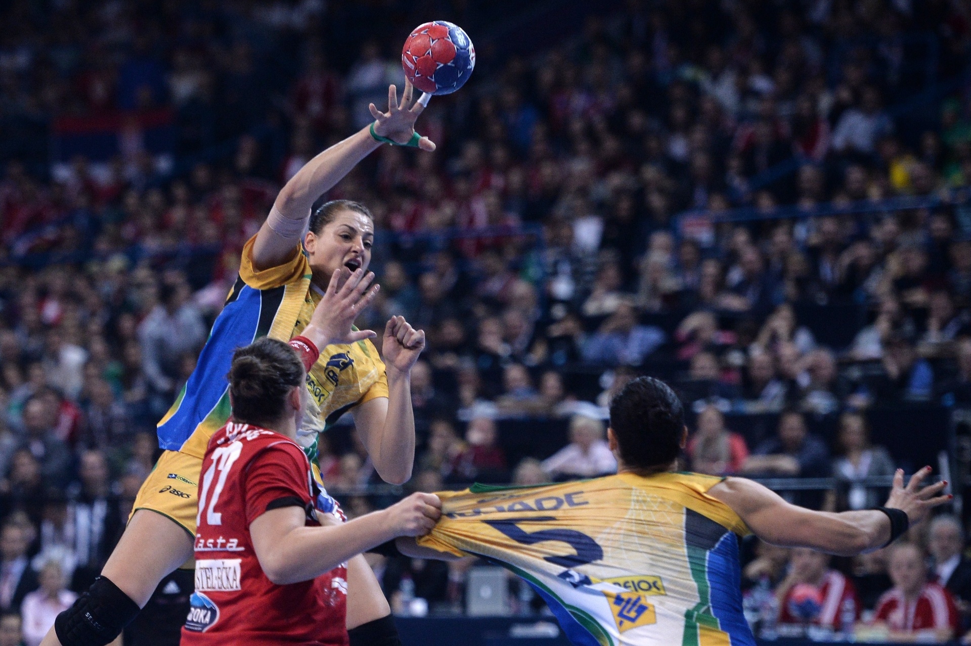 22.dez.2013 - Daniela tem camisa puxada por jogadora sérvia, enquanto Duda Amorim pula para arremessar bola na decisão do Mundial de Handebol - AFP PHOTO / DIMITAR DILKOFF