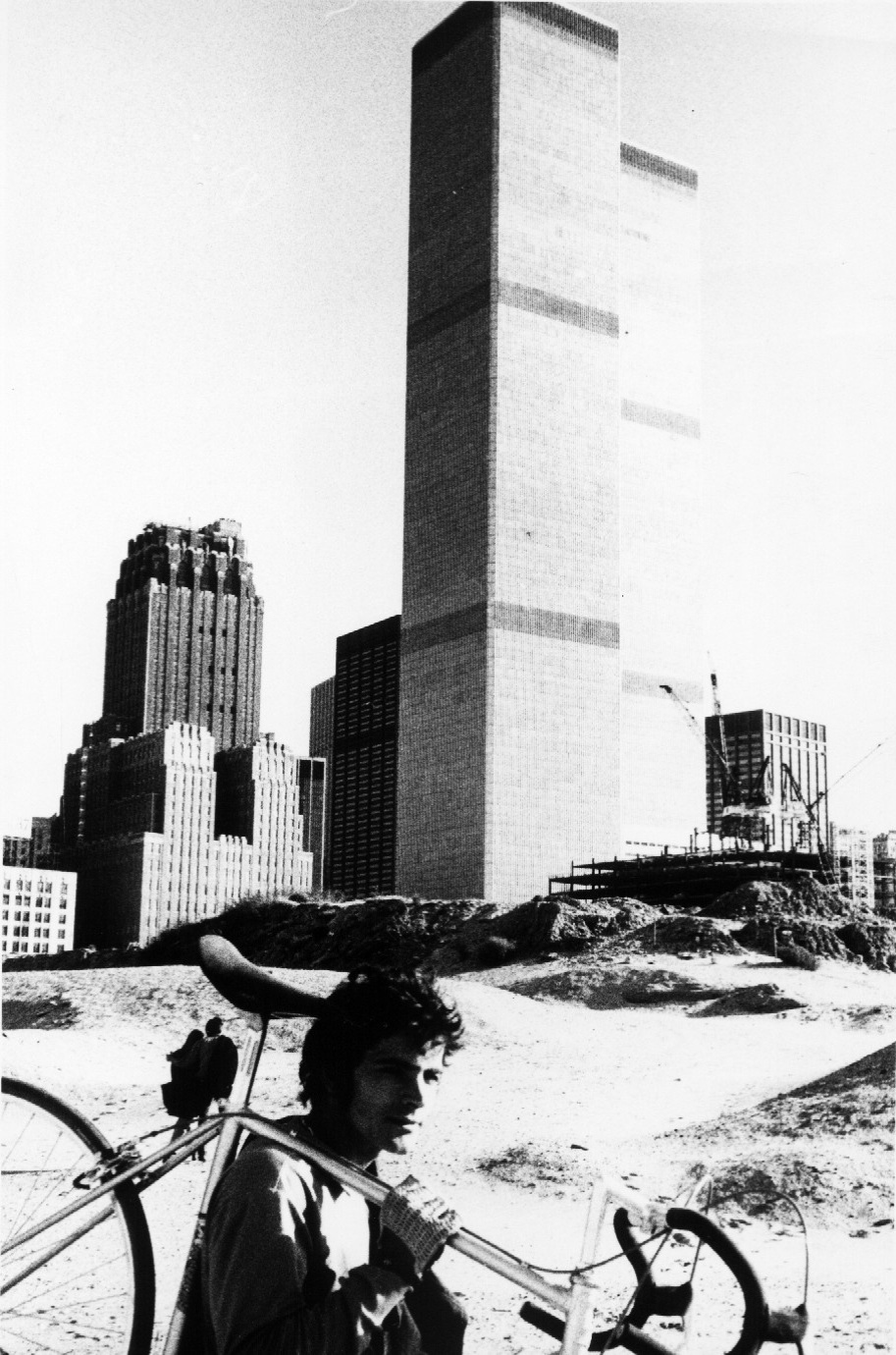 O mineiro carrega sua bicileta; no fundo a fachada do World Trade Center em NY