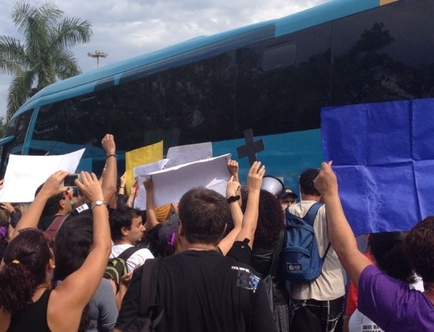Manifestantes apontam cartazes em direção a jogadores da seleção que estão dentro do ônibus. Colantes foram grudados no veículo em protesto à realização da Copa no país