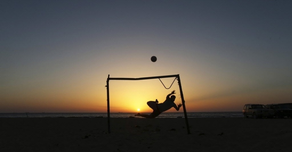 Garoto salta enquanto brinca em um campinho de areia na praia em Benghazi, na Líbia