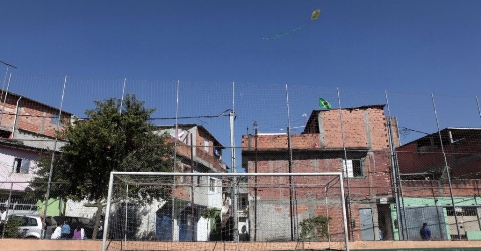 Uma pipa flutua no ar ao lado de um campinho em uma favela de São Paulo