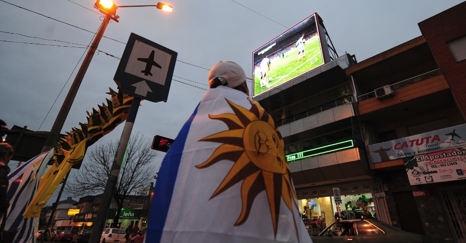 14.jun.2014 - Torcedor enrolado em bandeira uruguaia acompanha jogo contra Costa Rica em telão nas ruas de Rivera, fronteira com o Brasil no Rio Grande do Sul