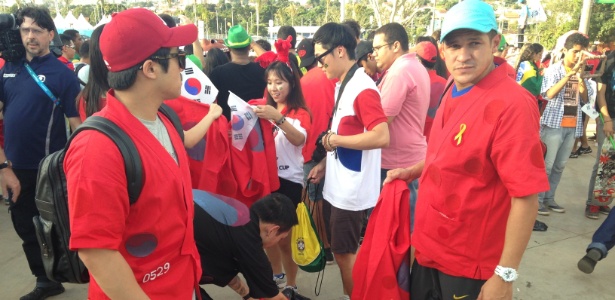 17.jun.2014 - O sul-coreano Kim Mim Kyu (de boné vermelho) e o brasileiro Willian Moura (de boné branco) ajudam a distribuir roupas para aumentar a torcida da Coreia do Sul em jogo da Copa do Mundo, em Cuiabá