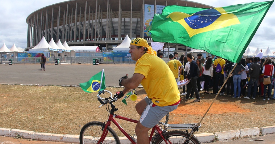 Torcedor passa de bicicleta próximo da entrada do estádio Mané Garrincha, que recebe partida entre Brasil x Camarões