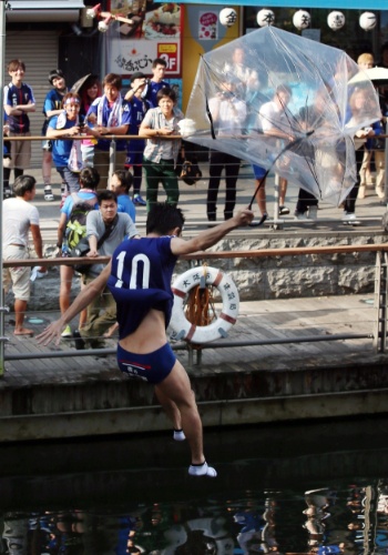 24.jun.2014 - Torcedor do Japão pula de guarda-chuva em rio da cidade de Osaka após derrota da seleção nacional para a Colômbia
