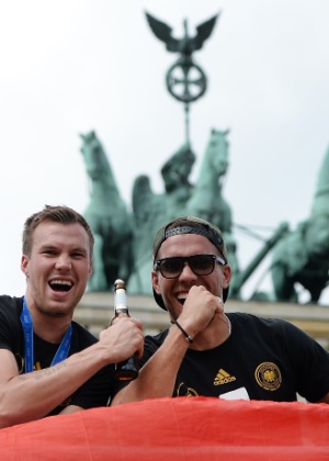 Ein prosit! Ou "um brinde", em português. Com cerveja na mão, Kevin Grosskreutz e Lukas Podolski chegam ao palco de comemoração do título, em frente ao Portão de Brandenburgo - AFP