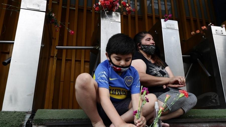 25.11.2020 - Criança posiciona flores na entrada do estádio La Bombonera, do Boca Juniors, em Buenos Aires, como homenagem a Maradona - Alejandro Pagni/AFP