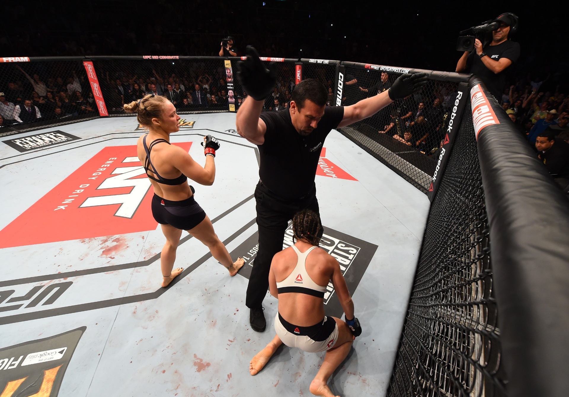 Ronda Rousey (esq.) comemora após nocautear Bethe Correia, que fica ajoelhada no chão, na luta principal do UFC 190 - Josh Hedges/Zuffa LLC UFC