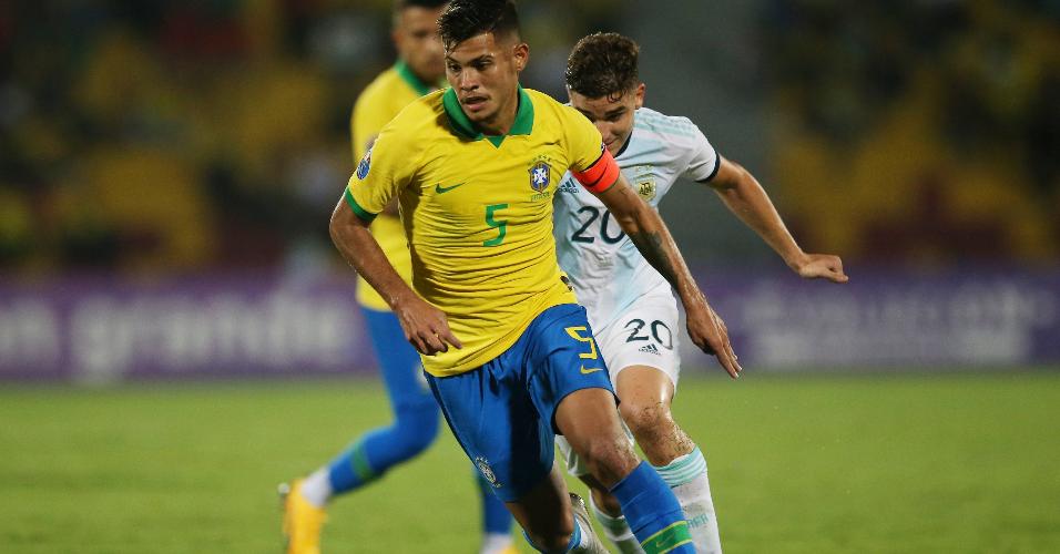 Capitão do Brasil, Bruno Guimarães carrega a bola no jogo contra a Argentina no Pré-Olímpico