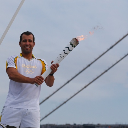 Bruno Fontes, velejador brasileiro, exibe a tocha olímpica em um barco em Florianópolis