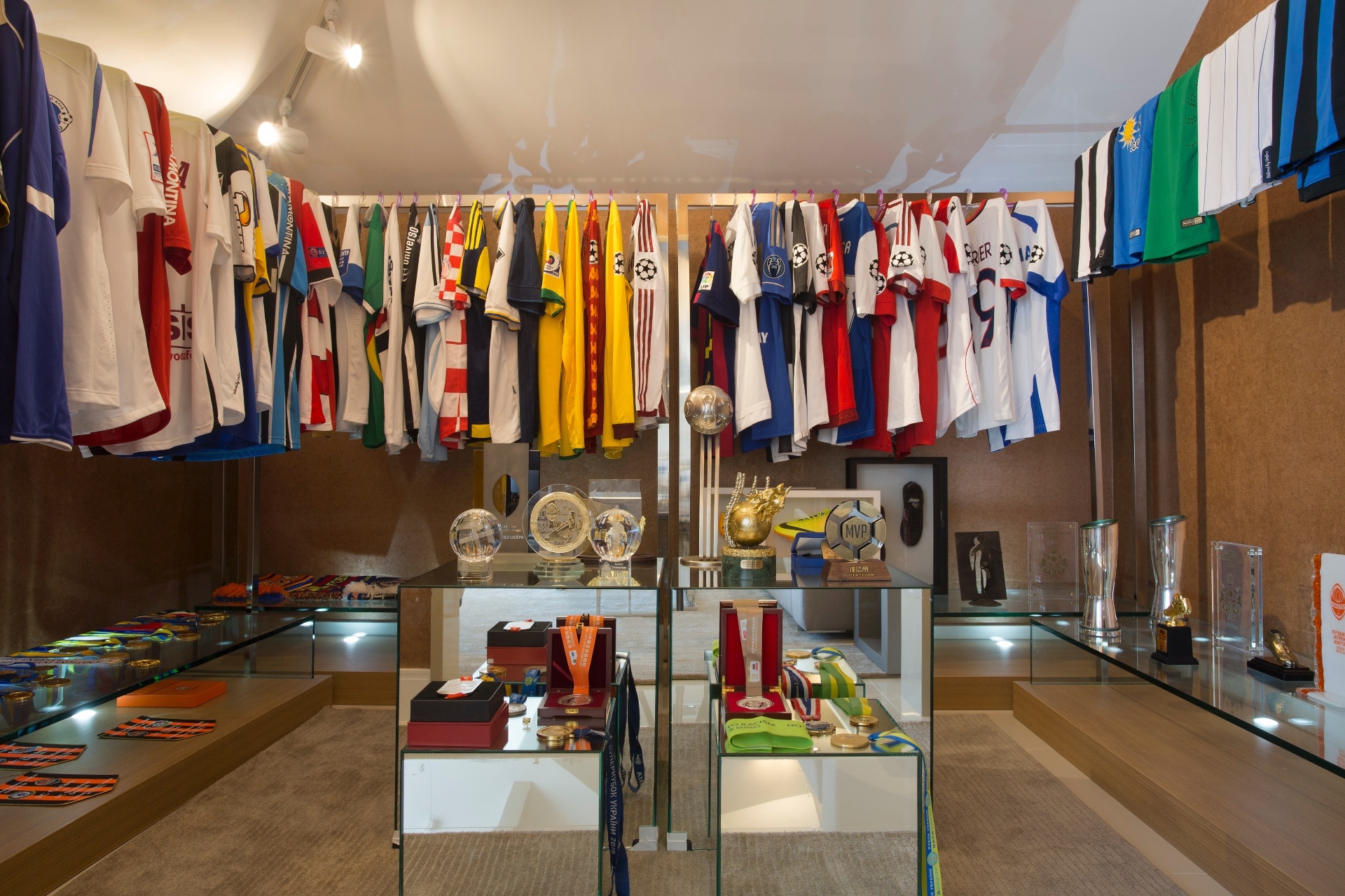 Sala de troféus da casa de Alex Teixeira tem lembranças importantes da carreira do jogador expostas como as camisas nas araras e as chuteiras. Medalhas e troféus estão dispostos em tótens no centro - Divulgação