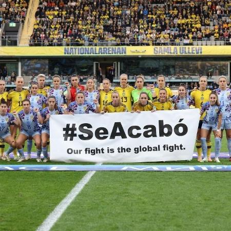 Jogadoras de Suécia e Espanha com a faixa "#acabou-se A nossa luta é a luta global"