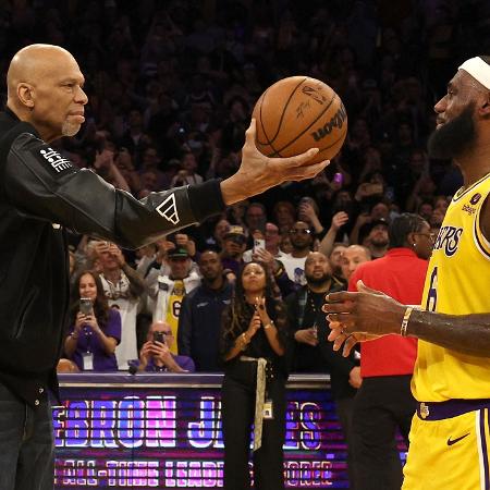 Kareem Abdul-Jabbar entrega bola de basquete a LeBron James, simbolizando a quebra do recorde de mais pontos na história da NBA. - Harry How/Getty Images