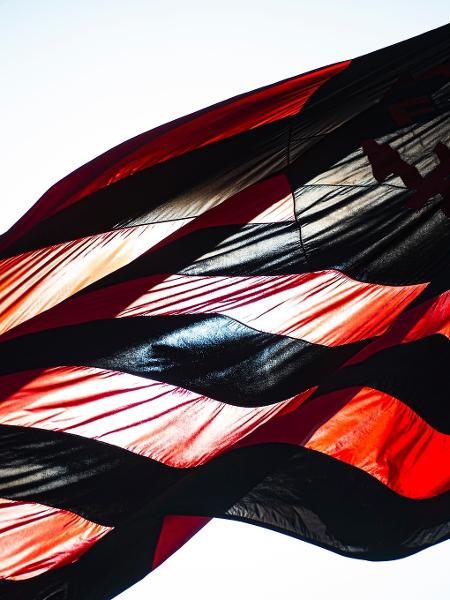 Bandeira do Flamengo tremulando sob sol forte, no Ninho do Urubu