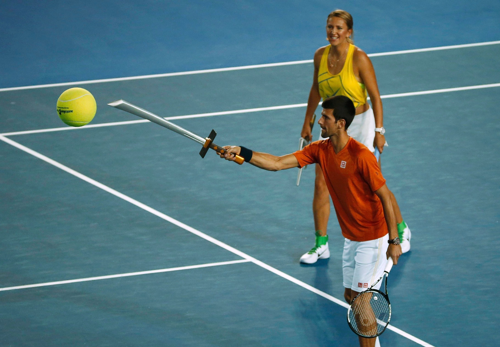 O sérvio Novak Djokovic ataca a bola com uma nova raquete... não, péra! É só uma espada de brinquedo usada em evento para crianças no Aberto da Austrália - Reuters