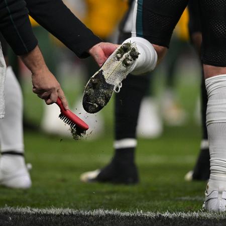 Funcionário do Philadelphia Eagles tira grama da chuteira de jogador durante jogo da NFL no Brasil