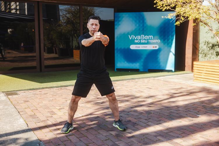 Em pé, abra as pernas em uma largura igual a entre os ombros e flexione levemente os joelhos. Estenda os braços à frente do corpo entrelaçando as mãos. Contraia os músculos das pernas, costas e do abdome, como você faria em uma prancha abdominal.